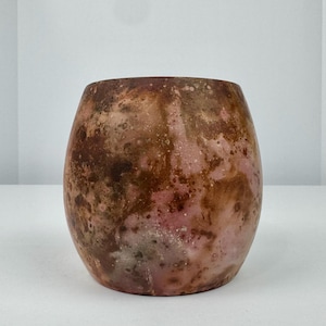 May include: A handcrafted, oval-shaped ceramic vase with a mottled, earthy color palette. The vase features shades of brown, pink, and hints of green, creating a unique, organic appearance. The surface has a textured, speckled finish, adding to its rustic charm.