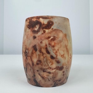 May include: A cylindrical ceramic vase with a unique marbled design. The vase features a blend of brown, beige, and reddish-orange hues, creating a textured, organic appearance. The vase is approximately 5 inches tall.