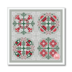 May include: A framed cross-stitch piece featuring four square panels with red, green, and white geometric designs. The designs include snowflake and floral patterns on a gray background. The piece is framed in white and includes a small logo in the bottom right corner.