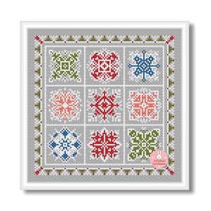 May include: A framed cross-stitch piece featuring nine square panels with snowflake designs in red, green, blue, and pink. The piece has a gray background and a white frame. The text "Stitched Sunbeams" is in the lower right corner.