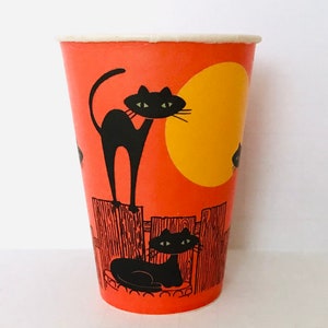 May include: Orange paper cup with a black cat design. The cup features a black cat standing on a fence, a yellow moon, and a sleeping cat. The cup has a white rim and is likely for Halloween.
