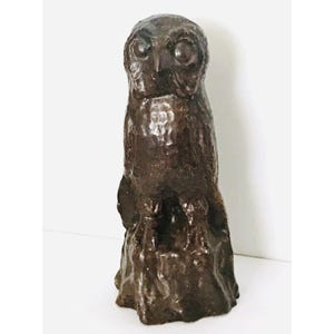 May include: A dark brown ceramic owl sculpture perched on a textured base. The owl has large, round eyes and a detailed beak.