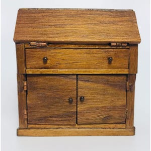 Puede incluir: Un armario de madera con una tapa abatible, un cajón y dos puertas. El armario está teñido de un color marrón oscuro y tiene herrajes de metal negro.