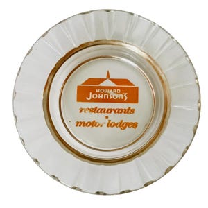 May include: White glass ashtray with a gold rim and an orange logo that reads "Howard Johnson's restaurants motels lodges".