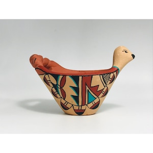 May include: Hand-painted ceramic bird-shaped bowl. The bowl is primarily tan with red, black, and turquoise geometric designs. The bird's head is a lighter tan colour. The bowl is likely used for decorative purposes.