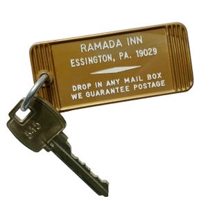 May include: A gold key tag with the text "RAMADA INN ESSINGTON, PA. 19029 DROP IN ANY MAIL BOX WE GUARANTEE POSTAGE" and a key attached to it.