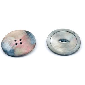 May include: Two round buttons. One button is a mix of pink, blue, and cream colors with four holes. The other button is a silver color with a pearlescent sheen and two holes.