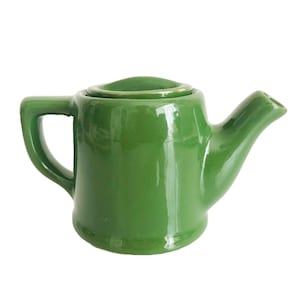 May include: A small, glossy green ceramic teapot with a handle and spout. The lid sits on top of the pot. The teapot is a solid, vibrant green colour and is likely used for brewing tea. The design is simple and classic.