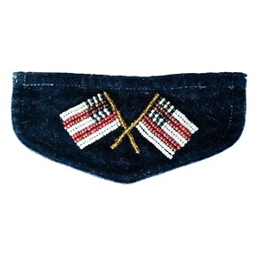 May include: A navy blue felt patch with two crossed flags. The flags are made with red, white, and black beads, and the flagpoles are gold. This decorative patch could be used on clothing or accessories.