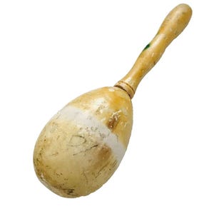 Puede incluir: Una maraca de madera vintage con un mango marr&oacute;n claro y un cuerpo en forma de huevo. El cuerpo tiene una banda blanca y muestra signos de desgaste. La maraca es un instrumento musical, probablemente utilizado para el ritmo y la percusi&oacute;n.