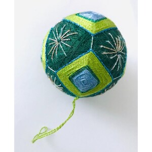 Könnte beinhalten: Ein handgenähtes Ornament in Grün und Blau mit geometrischem Muster und Stickerei aus silbernem Garn.