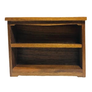 May include: A small, two-shelf wooden bookcase with a dark brown finish. The miniature bookshelf has a rectangular shape and is designed for decorative purposes. The shelves are evenly spaced, and the wood grain is visible.