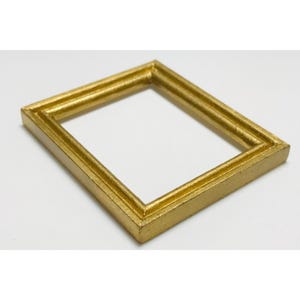 May include: A small, square, gold-colored picture frame. The frame has a layered design and is set against a white background. The frame is empty, ready for a photo or artwork.