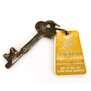 May include: A vintage key with a heart-shaped head and a tag. The key is rusty and worn, attached to a yellow tag with text that reads "WINDSOR HOTEL 1170 PEEL STREET MONTREAL-CANADA".