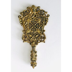 May include: An ornate hand mirror with a decorative handle and a floral design, finished in gold.