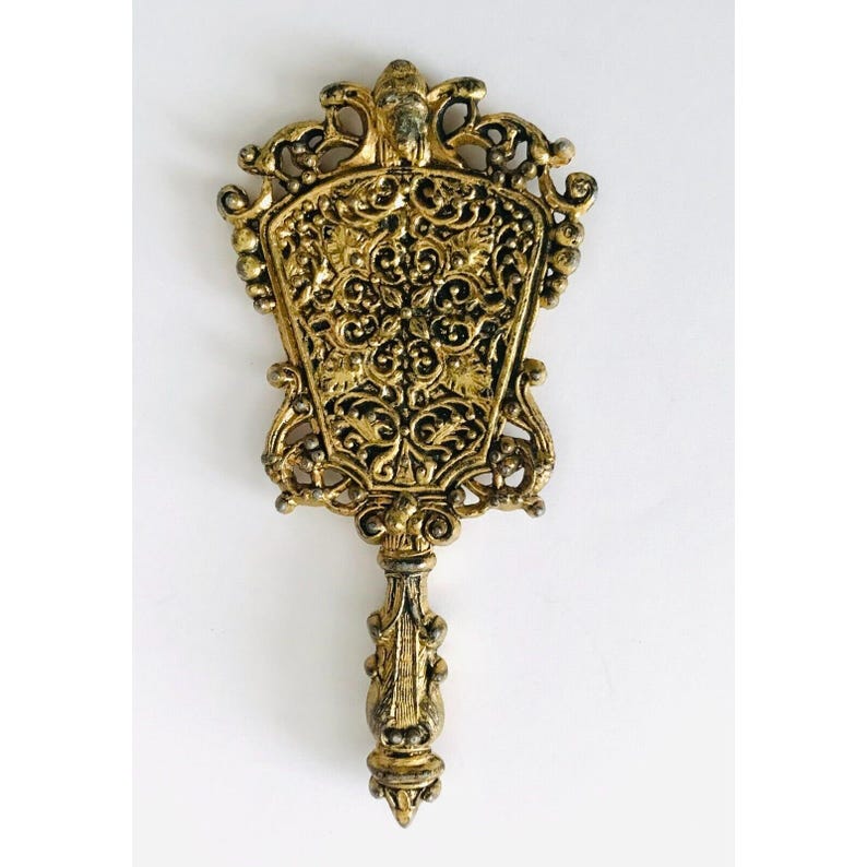 May include: An ornate hand mirror with a decorative handle and a floral design, finished in gold.