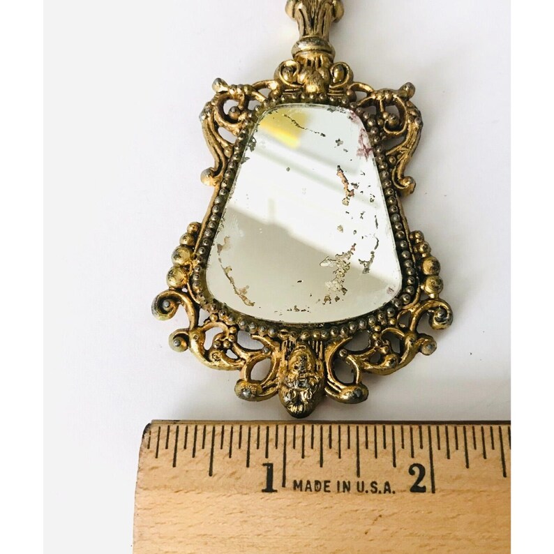 May include: An ornate hand mirror with a gold-toned finish and a bevelled glass mirror. The mirror is approximately 2.5 cm wide.