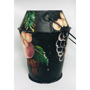 Könnte beinhalten: Schwarzer Metalleimer mit Henkel, bemalt mit bunten Obst- und Blumendesigns. Der Eimer ist etwa 18 cm hoch.