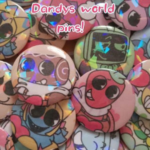 May include: A collection of colorful, round pins with holographic accents. Each pin features a unique cartoon character design in various colors, including pink, blue, and green. The text "Dandys world pins!" is displayed in pink cursive.