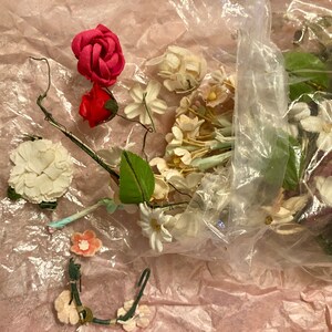 Op de afbeelding: Een plastic zak gevuld met verschillende kunstbloemen, waaronder roze rozen, witte madeliefjes en groene bladeren. De bloemen zijn losjes en natuurlijk gerangschikt, en de zak is open aan de bovenkant, waardoor de inhoud zichtbaar is.