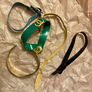 Op de afbeelding: Een verzameling van vier verschillende armbanden, waaronder een tealblauwe armband met gouden accenten, een groene armband met gouden accenten, een gouden armband en een zwarte armband.