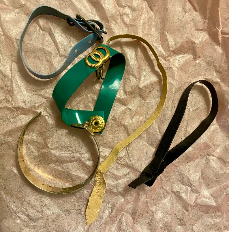 Op de afbeelding: Een verzameling van vier verschillende armbanden, waaronder een tealblauwe armband met gouden accenten, een groene armband met gouden accenten, een gouden armband en een zwarte armband.