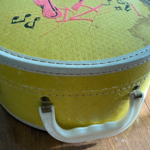May include: A yellow round hat box with a white handle and a white trim around the top. The lid has a pink and red design with musical notes and the words "Let's Have Fun".