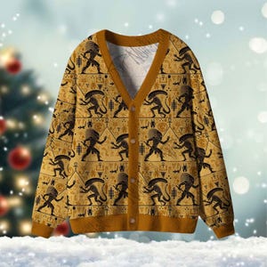 Könnte beinhalten: Eine Strickjacke mit Knöpfen und einem sich wiederholenden Muster aus schwarzen Alienfiguren und hieroglyphischen Symbolen auf beigem Hintergrund. Die Strickjacke hat braune Verzierungen und Knöpfe. Der Hintergrund ist eine verschwommene Winterszene mit einem Weihnachtsbaum.