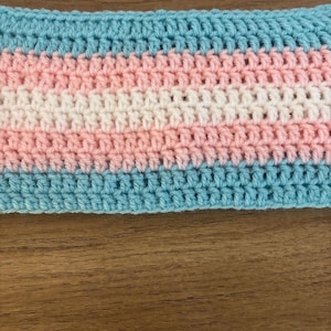 May include: A crocheted item in the colours of the transgender pride flag: light blue, pink, and white. The handmade piece has a horizontal striped pattern, with each colour forming distinct bands. The texture shows the individual crochet stitches.