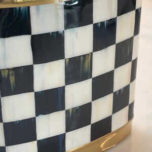 May include: A decorative container with a black and white checkered pattern. The top and base are trimmed with a gold-colored metal. The container has a glossy finish and a rounded rectangular shape.