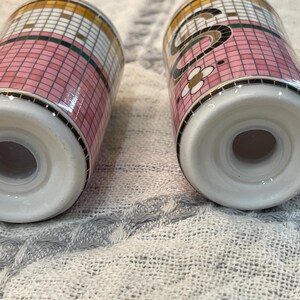 Puede incluir: Dos saleros de cer&aacute;mica con un patr&oacute;n de mosaico rosa, blanco y dorado. Los saleros tienen una base blanca y un borde negro. Un salero tiene un dise&ntilde;o floral.