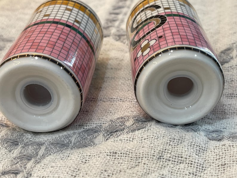 Puede incluir: Dos saleros de cer&aacute;mica con un patr&oacute;n de mosaico rosa, blanco y dorado. Los saleros tienen una base blanca y un borde negro. Un salero tiene un dise&ntilde;o floral.