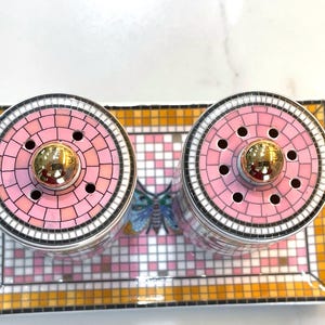 Puede incluir: Un juego decorativo de salero y pimentero con tapas de mosaico rosa y blanco y detalles dorados. El juego incluye dos saleros y una bandeja rectangular con un dise&ntilde;o de mariposa.