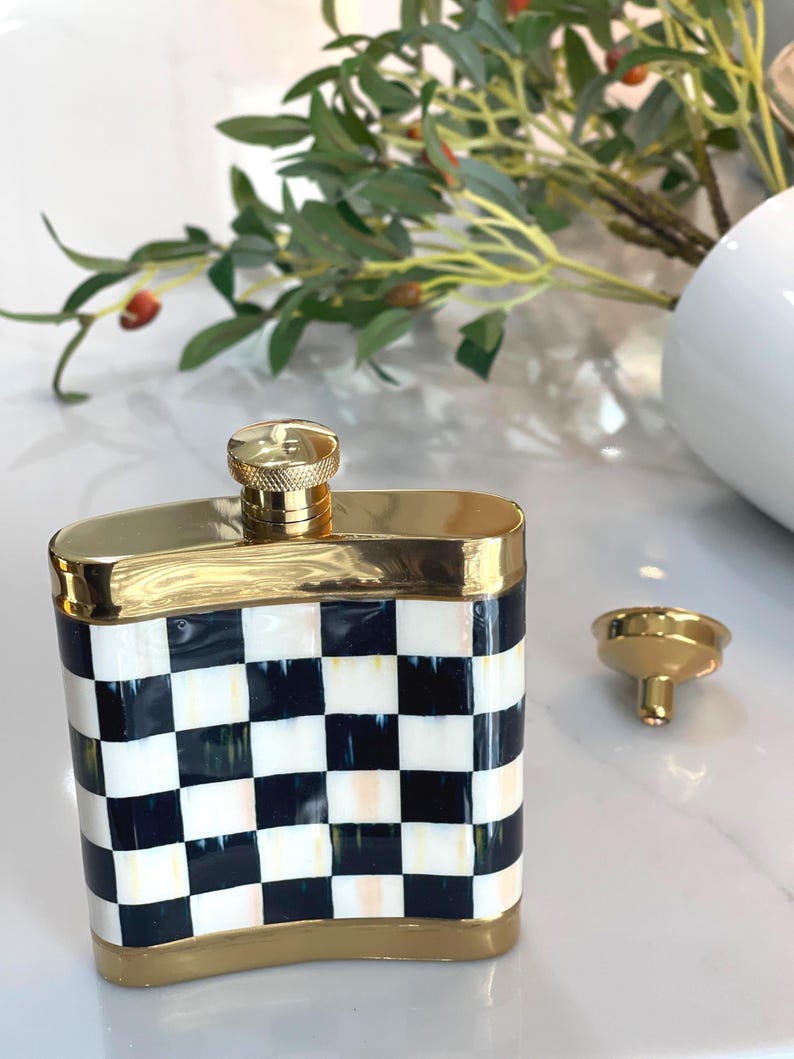 May include: A decorative flask with a gold-colored rim and cap. The flask features a black and white checkered pattern on the front and sides. A small gold funnel sits next to the flask.