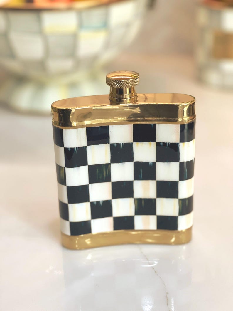May include: A decorative flask with a black and white checkered pattern. The flask has gold-colored trim around the top, bottom, and cap. The cap is also gold-colored. The flask is rectangular in shape.