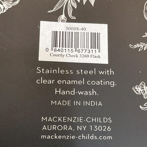 May include: Close-up of a product label with the text "Courtly Check 3260 Flask." The label includes a barcode and the words "Stainless steel with clear enamel coating. Hand-wash. Made in India." The brand name "MACKENZIE-CHILDS" is also visible.