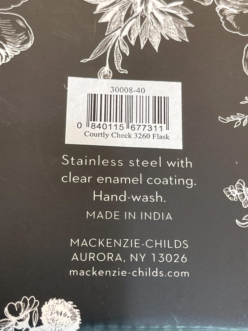 May include: Close-up of a product label with the text "Courtly Check 3260 Flask." The label includes a barcode and the words "Stainless steel with clear enamel coating. Hand-wash. Made in India." The brand name "MACKENZIE-CHILDS" is also visible.