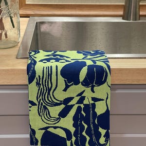 May include: A folded kitchen towel with a vibrant pattern of navy blue botanical shapes on a light green background. The towel is made of a soft fabric and has a striped border.