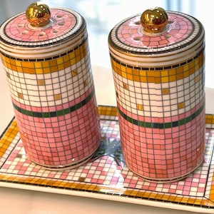 Puede incluir: Dos saleros y pimenteros decorativos de cer&aacute;mica con una bandeja a juego. Los saleros y la bandeja presentan un dise&ntilde;o de mosaico en rosa, blanco, dorado y verde. Cada salero tiene una tapa dorada.