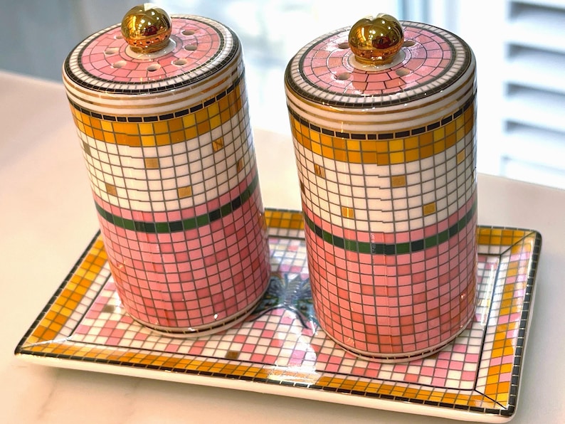 Puede incluir: Dos saleros y pimenteros decorativos de cer&aacute;mica con una bandeja a juego. Los saleros y la bandeja presentan un dise&ntilde;o de mosaico en rosa, blanco, dorado y verde. Cada salero tiene una tapa dorada.