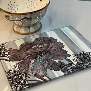 Puede incluir: Bandeja rectangular de vidrio para servir con un dise&ntilde;o floral en tonos marr&oacute;n y gris. La bandeja tiene un fondo a rayas y est&aacute; decorada con ilustraciones bot&aacute;nicas. Un colador decorativo est&aacute; en el fondo.