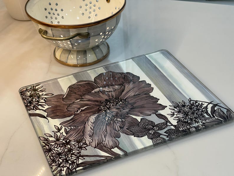 Puede incluir: Bandeja rectangular de vidrio para servir con un dise&ntilde;o floral en tonos marr&oacute;n y gris. La bandeja tiene un fondo a rayas y est&aacute; decorada con ilustraciones bot&aacute;nicas. Un colador decorativo est&aacute; en el fondo.