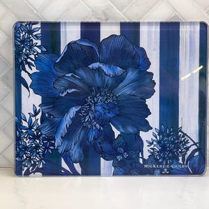 May include: Rectangular glass serving tray with a blue floral design and vertical blue and white stripes. The tray features a large blue flower and smaller floral accents. The brand name "McKENZIE-CHILDS" is printed on the bottom right.