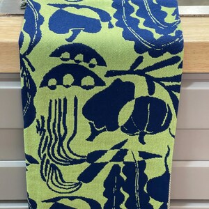 May include: A kitchen towel with a repeating pattern of dark blue organic shapes on a light green background. The towel is hanging on a silver bar. The towel's border is a light gray and white striped pattern.