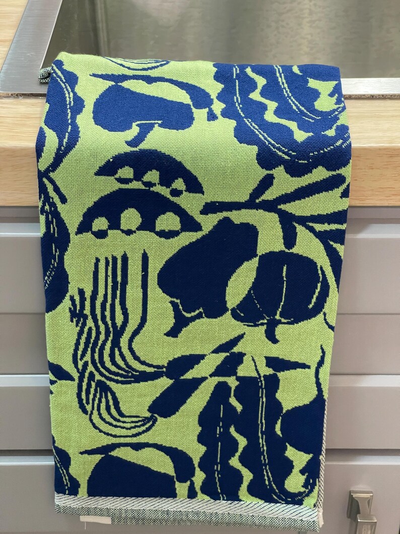 May include: A kitchen towel with a repeating pattern of dark blue organic shapes on a light green background. The towel is hanging on a silver bar. The towel's border is a light gray and white striped pattern.