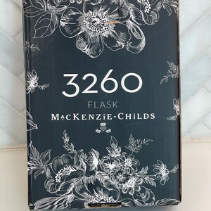 May include: A dark gray flask box with white floral illustrations. The number "3260" is centered in white, with "FLASK" and "MACKENZIE-CHILDS" below. The box has a decorative floral design.