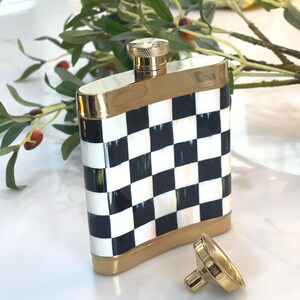 May include: A decorative flask with a black and white checkered pattern. The flask has gold-colored trim and a matching gold cap. The cap is detached and lying next to the flask. The flask is rectangular and has rounded edges.