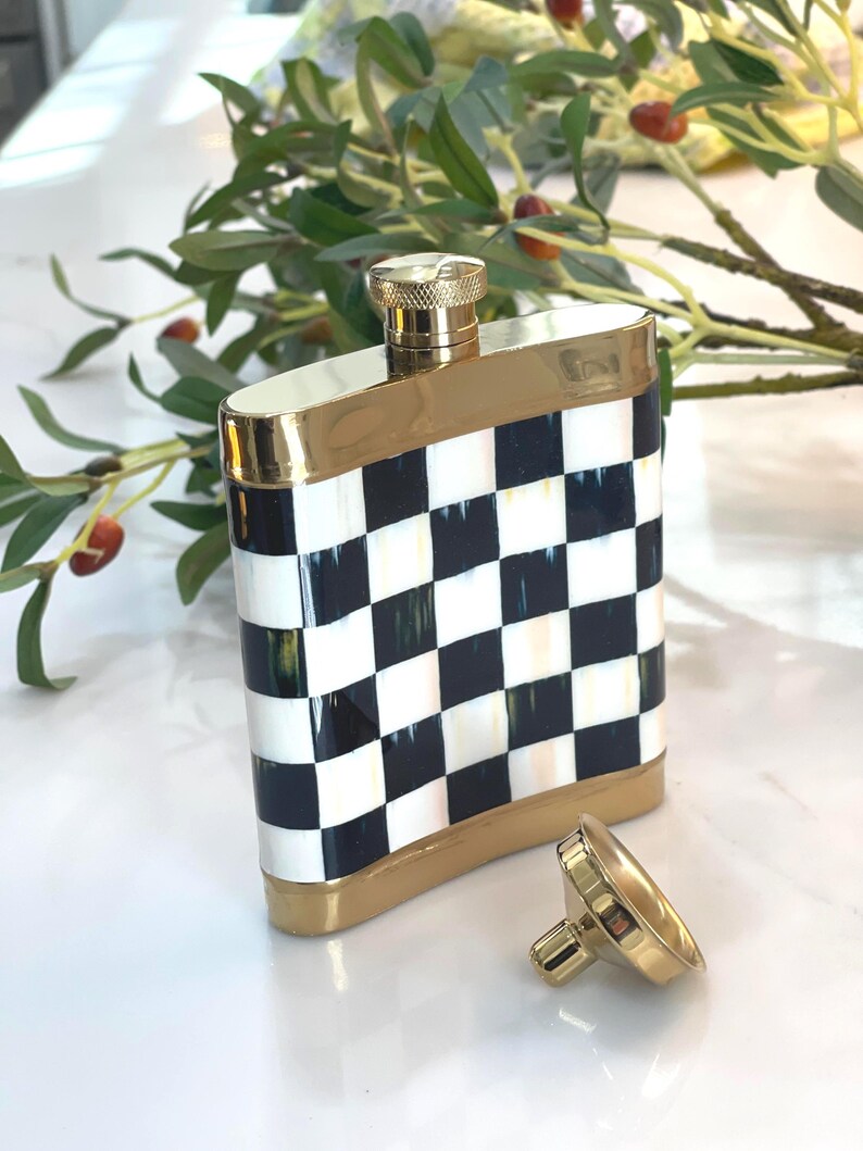 May include: A decorative flask with a black and white checkered pattern. The flask has gold-colored trim and a matching gold cap. The cap is detached and lying next to the flask. The flask is rectangular and has rounded edges.
