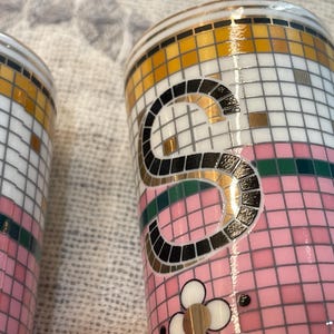 Puede incluir: Dos vasos decorativos de cer&aacute;mica con un dise&ntilde;o de mosaico. Los vasos presentan una combinaci&oacute;n de colores rosa, blanco, dorado y negro. La letra "S" se muestra de forma destacada en un vaso y se ve un dise&ntilde;o floral.