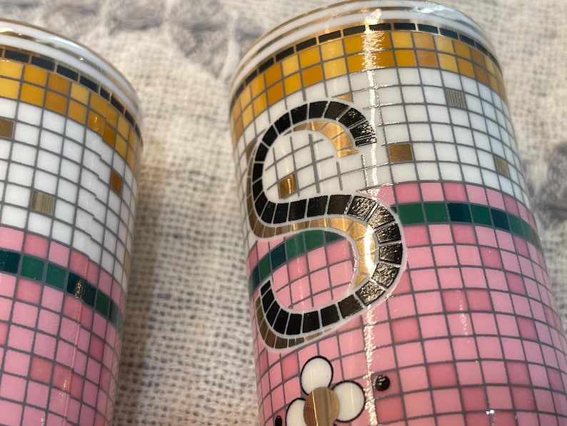 Puede incluir: Dos vasos decorativos de cer&aacute;mica con un dise&ntilde;o de mosaico. Los vasos presentan una combinaci&oacute;n de colores rosa, blanco, dorado y negro. La letra "S" se muestra de forma destacada en un vaso y se ve un dise&ntilde;o floral.